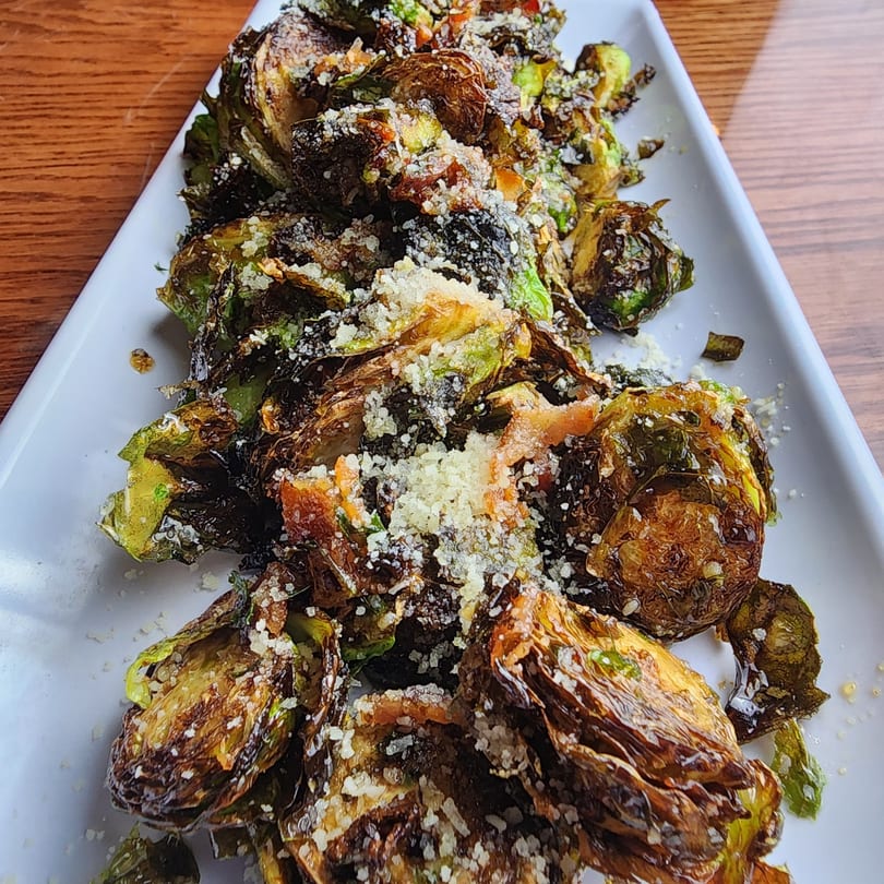 Crispy roasted Brussels sprouts with parmesan cheese on a white rectangular plate at Rock N Roll Meatballs.