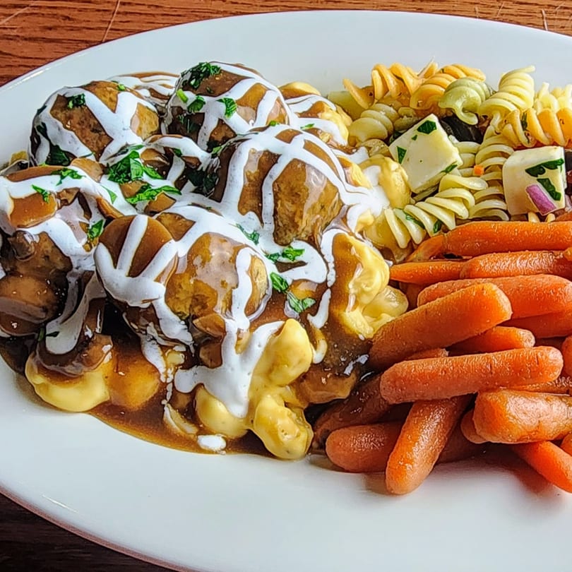 Meatballs with gravy and white sauce, served with macaroni and cheese, pasta salad, and baby carrots.