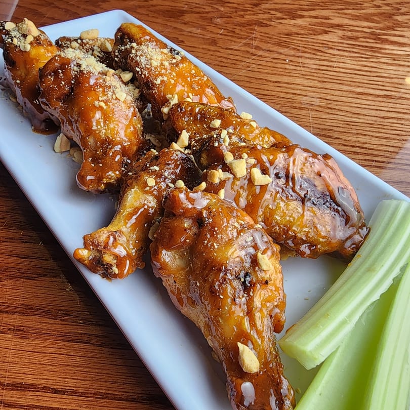 Sweet and spicy chicken wings with peanuts and celery sticks on a white plate.