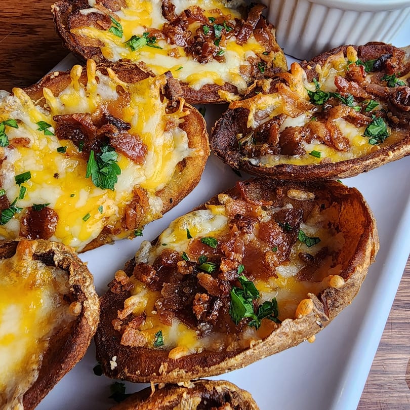 Six crispy potato skins filled with melted cheese, bacon bits, and fresh parsley on a white plate.