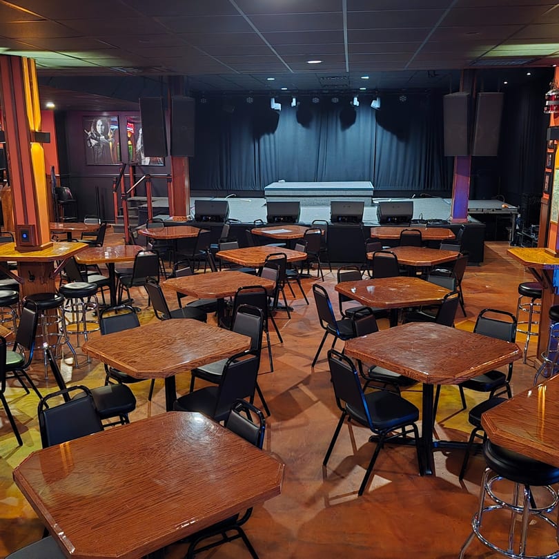 Empty Rock N Roll Meatballs bar-and-grill dining room with tables, chairs, and a stage.