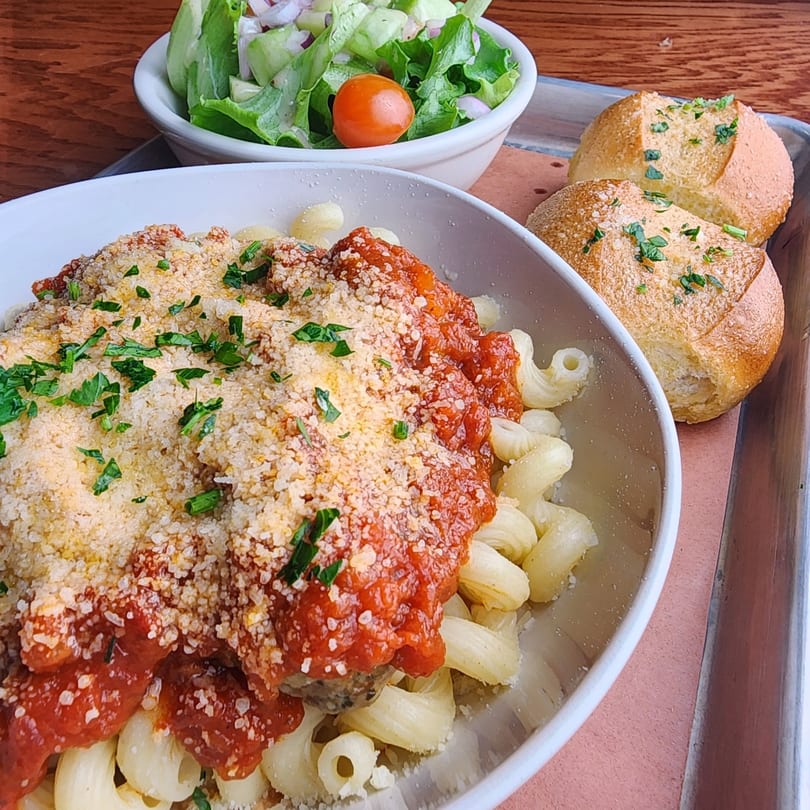 Rock N Roll Meatballs' pasta with red sauce, parmesan, and parsley, served with a side salad and bread.